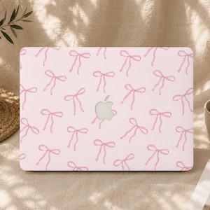 Può includere: Una custodia rigida per laptop color rosa chiaro con un motivo ripetuto di piccoli fiocchi rosa disegnati a mano. Il centro della custodia presenta un ritaglio per il logo Apple argentato, visibile attraverso il centro del design.