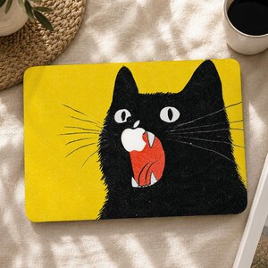 Pode incluir: Um adesivo retangular para portátil com um fundo amarelo vibrante e uma grande ilustração de um gato preto. O gato tem olhos arregalados, bigodes longos e a boca aberta revelando uma forma de logótipo de maçã branca.