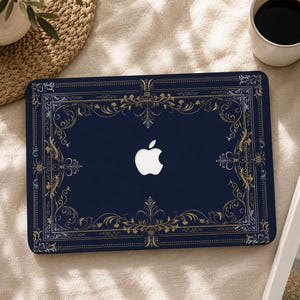 Peut inclure: Un autocollant pour ordinateur portable bleu marine foncé orné d'une bordure en filigrane doré complexe encadrant les bords. Le motif présente des volutes florales symétriques et une découpe centrale révélant le logo Apple blanc de l'appareil.