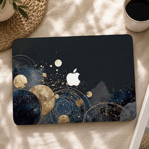 May include: A laptop cover featuring a dark navy blue and black watercolor background with gold circular motifs, thin gold line art rings, and gold speckles. The center of the cover displays a cutout for the white Apple logo.