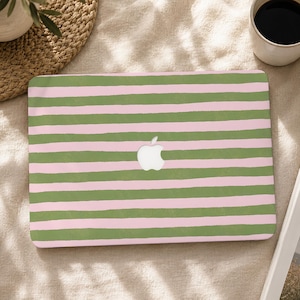 Può includere: Una skin per laptop con un motivo ripetitivo di strisce orizzontali dipinte a mano in tonalità alternate di verde salvia e rosa pastello tenue. Il design presenta un ritaglio centrale che rivela il logo Apple argentato sul coperchio.