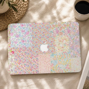 May include: A laptop skin featuring a patchwork design of various floral patterns in pastel shades of pink, yellow, blue, and green. The rectangular cover has a central cutout revealing the white Apple logo on the laptop surface beneath the skin.