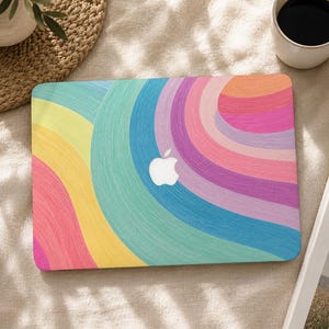 Op de afbeelding: Een laptopskin met een levendig, meerkleurig patroon van gebogen, getextureerde lijnen in tinten geel, teal, roze, oranje en paars. Het ontwerp straalt naar buiten uit en creëert een wervelend effect over het rechthoekige oppervlak.