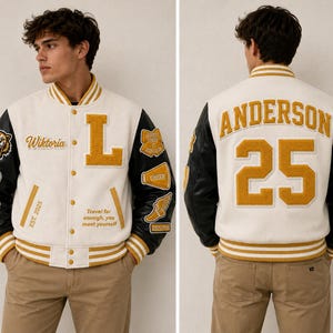 Può includere: Una giacca varsity con corpo bianco e maniche nere, caratterizzata da bordi a coste a righe gialle e bianche. Il davanti mostra il nome Wiktoria, una grande lettera L e il testo Travel far enough, you meet yourself. Il retro presenta il nome ANDERSON e il numero 25 in giallo.