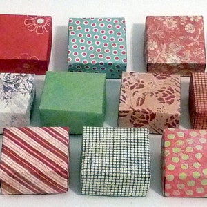 May include: A collection of small, square gift boxes with various patterned designs. The boxes feature floral, star, plaid, and polka dot patterns in colors like red, green, blue, and beige. The boxes are arranged in rows, showcasing the variety of designs.