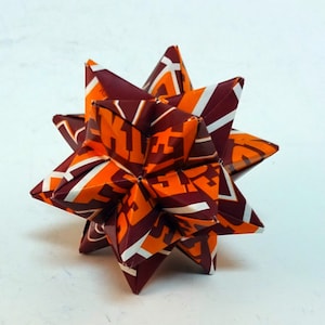 Könnte beinhalten: Ein brauner und orangefarbener Origami-Stern mit geometrischem Muster. Der Stern ist aus Papier mit einem sich wiederholenden Muster gefertigt.