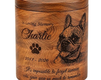 May include: A cylindrical wooden urn featuring a dark brown wood grain finish. The front is engraved with the text In Loving Memory, the name Charlie, a paw print, the years 2011-2026, a French Bulldog portrait, and the quote It's impossible to forget someone who gave you so much to remember.