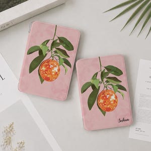 May include: Two rectangular tablet cases in a soft pink hue, each featuring a graphic illustration of a hanging orange disco ball fruit with green leaves. The smaller case displays the name Joshua in a black script font in the bottom corner.