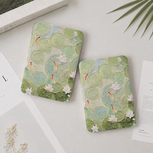 Puede incluir: Dos fundas rectangulares para tablet con un diseño de pintura al óleo impresionista de nenúfares verdes, flores blancas y pequeños peces koi naranjas nadando. La funda más pequeña incluye el nombre Joshua impreso en letra cursiva negra.