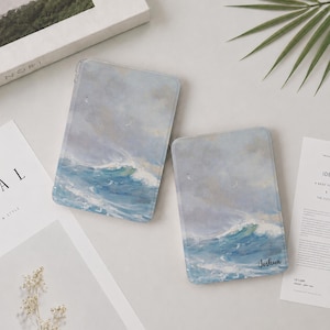 May include: Two rectangular e-reader cases featuring an oil painting style print of a turbulent ocean with crashing blue and white waves under a cloudy sky. The smaller case includes the name Joshua printed in a black script font in the corner.