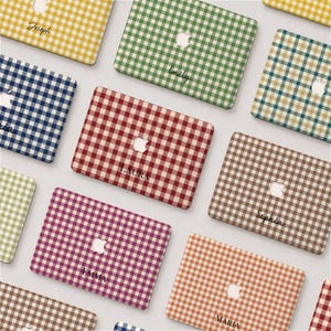 May include: A collection of rectangular laptop cases featuring a gingham check pattern in various colors including yellow, green, blue, red, brown, purple, and orange. Each case displays a central Apple logo cutout and a personalized name.