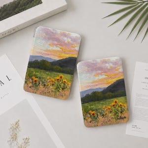 May include: Two rectangular tablet cases featuring an oil painting style landscape of a sunflower field under a pink and orange sunset sky. The right case includes the name Joshua printed in a black script font near the bottom right corner.