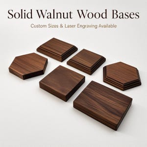 Può includere: Sei basi in legno di noce massello di forma quadrata, rettangolare ed esagonale con profili dei bordi variabili. Il testo "Solid Walnut Wood Bases" e "Custom Sizes & Laser Engraving Available" è visualizzato nella parte superiore.