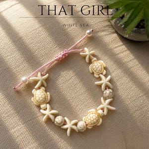 Puede incluir: Una pulsera con dijes de tortugas marinas y estrellas de mar en color crema, intercalados con cuentas de mármol blanco en un cordón rosa. Incluye cordones ajustables con pequeñas cuentas blancas en los extremos. Texto: JEWELRY THAT GIRL WHITE SEA.