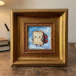 May include: A small oil painting in a thick gold frame depicting a smiling slice of toast with a red and blue backpack against a light blue sky with white clouds. The toast has a tan crust, a light center, and small arms and legs.