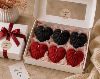 May include: A white gift box containing six heart-shaped candles with a textured, woven-like surface. Three candles are black and three are red, all nestled in light pink tissue paper. The box lid features a clear window and a sticker reading handmade with love.