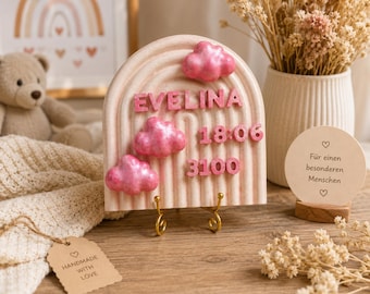 May include: A semi-circular beige plaque with a textured ribbed pattern, featuring the name EVELINA in pink letters, three pink metallic clouds, and the numbers 18:06 and 3100 in pink, all supported by a small gold-toned metal display stand.