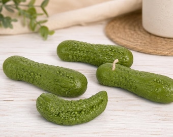 May include: Three green pickle-shaped candles with textured, bumpy surfaces. One candle features a visible white wick at the top. The candles are arranged in a cluster, displaying realistic details including small bumps and a deep green color.