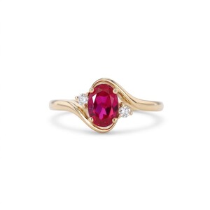 Puede incluir: Un anillo de oro con un rubí rojo central de talla ovalada sujeto por cuatro garras. La banda se curva alrededor de la piedra central, adornada con dos pequeños diamantes blancos de talla redonda, uno a cada lado del rubí en diseño cruzado.