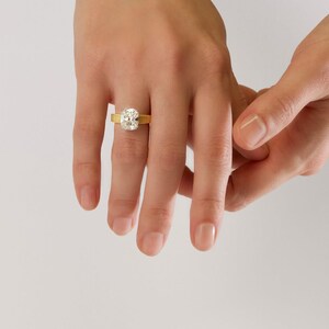 Peut inclure: Une bague en or orn&eacute;e d'une grande pierre transparente de taille coussin rectangulaire au centre. L'anneau de la bague pr&eacute;sente une finition distincte, verticalement nervur&eacute;e ou textur&eacute;e, contrastant avec la surface lisse et facett&eacute;e.
