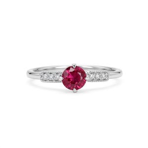 Puede incluir: Un anillo de plata con una piedra preciosa redonda de color rojo vibrante en el centro, flanqueada por dos secciones rectangulares en la banda, cada una con tres pequeñas piedras claras y brillantes con un detalle de borde milgrain.