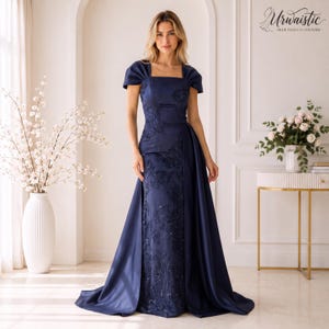 May include: A floor-length navy blue gown featuring a square neckline, short pleated sleeves, and a central panel adorned with tonal floral embroidery and beadwork. The dress includes a smooth, solid-coloured overskirt overlaying the embroidered base.