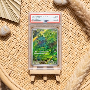 Könnte beinhalten: Eine bewertete 2023 Pokemon SV2a japanische Bulbasaur Art Rare Sammelkarte in einer durchsichtigen Kunststoffhülle. Die Karte zeigt ein grünes Wesen in einem dichten Wald mit dem Text Fushigidane und 70 KP. Das Etikett auf der Hülle lautet 2023 POKEMON SV2a JP BULBASAUR ART RARE GEM MT 10.