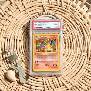 May include: A 1999 1st Edition French Charizard holographic trading card graded GEM MT 10, encased in a clear protective plastic slab. The card features a fire-type dragon illustration, 120 HP, and text detailing its attacks and abilities.