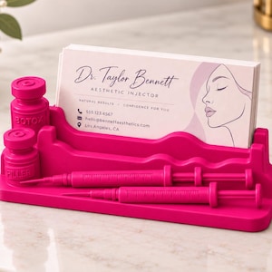 May include: A bright pink plastic business card holder featuring two molded vials labeled Botox and Filler, two syringe-shaped pens, and a stack of cards for Dr. Taylor Bennett, Aesthetic Injector, with contact details and a line-art face profile.