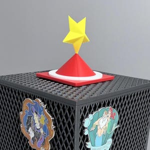 May include: A dark gray cubic display stand with a diamond-patterned mesh surface, topped with a red cone and a yellow star. Four enamel pins are attached to the sides, featuring animated characters including a mermaid, a dog, and various figures.