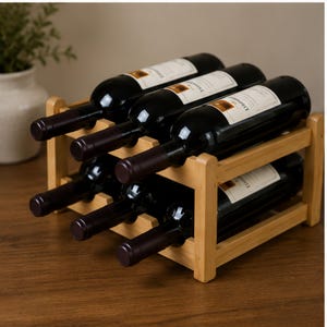 Puede incluir: Un botellero de madera clara que contiene seis botellas de vino de vidrio oscuro dispuestas en dos filas horizontales. Cada botella tiene una etiqueta rectangular blanca. El botellero tiene una estructura rectangular simple.