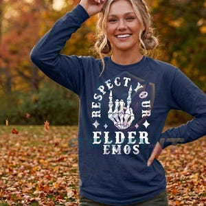 May include: A navy blue long-sleeve shirt featuring a white graphic of a skeleton hand making a rock-and-roll gesture. The text "RESPECT YOUR ELDER EMOS" is printed in white capital letters around the hand, accompanied by small four-pointed star icons.