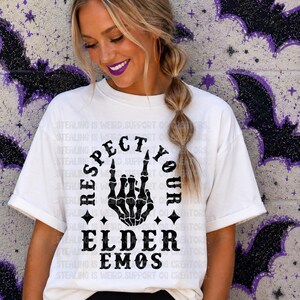 May include: A white short-sleeve t-shirt featuring a black graphic of a skeleton hand making a rock-and-roll gesture. The text "RESPECT YOUR ELDER EMOS" is printed in a bold, distressed black font surrounding the skeleton hand graphic.