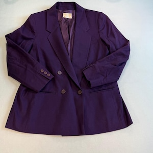 Puede incluir: Un blazer cruzado de color morado intenso con solapa de muesca, mangas largas con tres botones en cada puño y dos bolsillos delanteros ribeteados. La chaqueta está totalmente forrada con una tela morada a juego e incluye una etiqueta de marca.