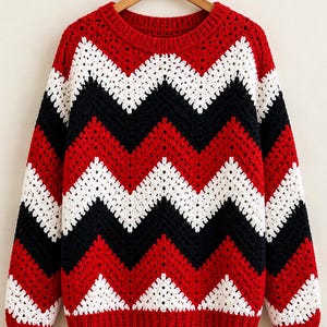 May include: A long-sleeve crochet sweater featuring a repeating chevron pattern in vibrant red, crisp white, and solid black. The garment has a round neckline and ribbed cuffs and hem, all constructed with a textured, open-stitch yarn design.