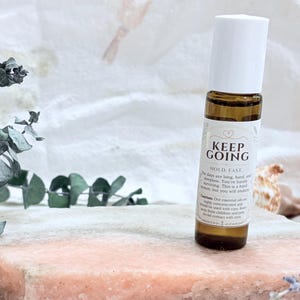 May include: A small amber glass roller bottle with a white cap and a label that reads KEEP GOING, HOLD. FAST. The days are long, hard, and sleepless. You're barely surviving. This is a hard season, but you will endure. Caution: Our essential oils are highly concentrated.