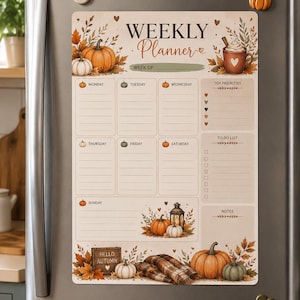 Op de afbeelding: Een magnetische weekplanner bevestigd aan een koelkast, met een herfstthema inclusief pompoenen, herfstbladeren en een mok cacao. De indeling bevat secties voor elke dag van de week, topprioriteiten, een takenlijst en notitieruimte.