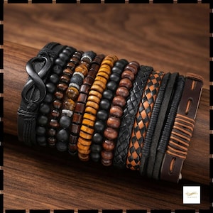 Op de afbeelding: Een meerlaagse armbandenset met een zwart oneindigheidssymbool op een leren band, diverse strengen zwarte, bruine en tijgeroogkralen, een gevlochten zwart leren koord, een geweven beige en zwarte leren band en een bruine leren manchet.