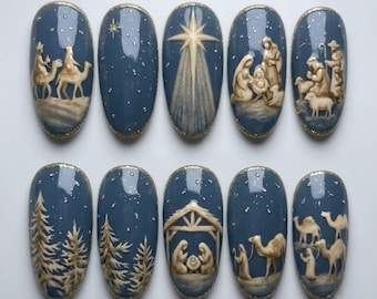 May include: A set of ten oval-shaped press-on nails featuring a dusty blue base with gold glitter accents. The designs depict a nativity scene, including figures of people, camels, sheep, a stable, pine trees, and a bright star, all rendered in cream-colored relief.