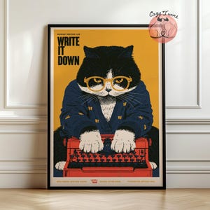 May include: A framed poster featuring a black and white cat wearing yellow-rimmed glasses and a navy blue cardigan, typing on a red typewriter. The background is mustard yellow with the text "WRITE IT DOWN" and "MIDNIGHT WRITERS CLUB".