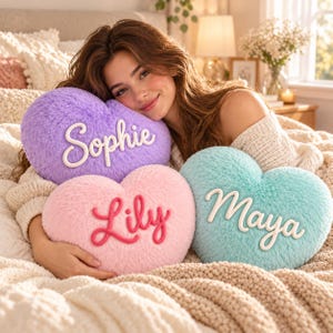 May include: Three heart-shaped plush pillows with fuzzy textures in purple, pink, and light blue. The purple pillow features the white embroidered name Sophie, the pink pillow has the red embroidered name Lily, and the light blue pillow displays the white embroidered name Maya.