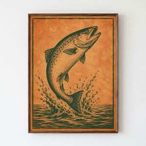May include: A framed wall art print featuring a dark green illustration of a fish leaping out of water against a textured orange background. The artwork is enclosed in a simple dark brown wooden frame, showcasing a detailed graphic design.