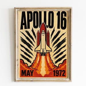 May include: A framed poster featuring a space shuttle launching with orange and red flames. The text APOLLO 16 is printed in large black letters at the top, and MAY 1972 is printed in black at the bottom against a cream-colored background.