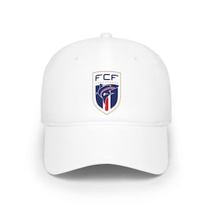 May include: A white baseball cap featuring a centered shield-shaped logo. The logo displays the text FCF in dark blue above a stylized shark graphic in blue and red, all enclosed within a gold-bordered crest design on the front panel.