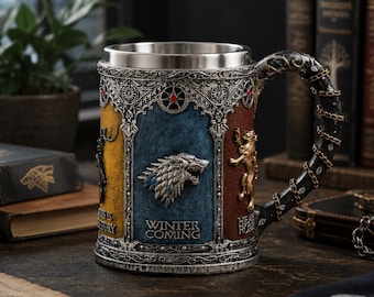 May include: A cylindrical tankard with a metallic silver rim and handle wrapped in a chain. The exterior features three colored panels: yellow with a stag, blue with a wolf head and the text WINTER IS COMING, and brown with a lion and text.