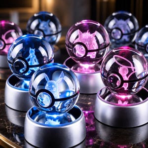 May include: A collection of spherical glass ornaments featuring laser-etched character figures inside. Each clear orb is designed to resemble a ball with a central black band and sits atop a circular silver base that illuminates the interior.