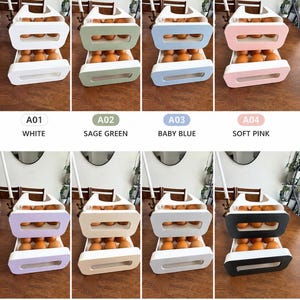 May include: A two-tiered rolling egg dispenser rack available in eight colors: white, sage green, baby blue, soft pink, lavender, sand beige, light gray, and black and white. Each unit features a rectangular frame with a front-facing cutout.