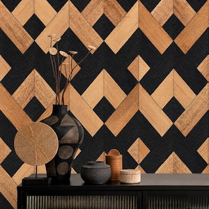 May include: A black vase with abstract shapes, a round tan textured disc on a stand, a small dark gray bowl, a tall tan cylindrical container, and a small tan ribbed container arranged on a black surface against a geometric wood and black wall.
