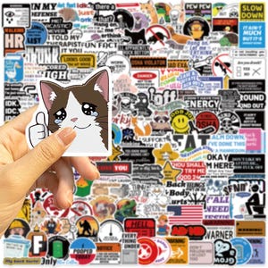 May include: A collection of assorted vinyl stickers featuring various graphic designs, text-based humour, and illustrations. One prominent sticker shows a brown and white cat with teary eyes giving a thumbs up, surrounded by numerous other stickers.