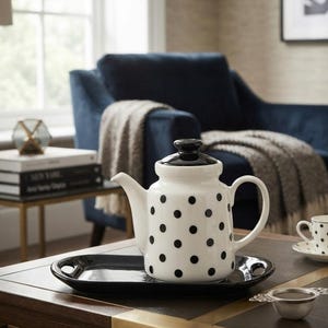 Peut inclure: Une théière en céramique blanche à pois noirs avec un couvercle noir uni, posée sur un plateau de service rectangulaire noir assorti doté de poignées intégrées. La théière présente un bec verseur incurvé et une anse latérale.